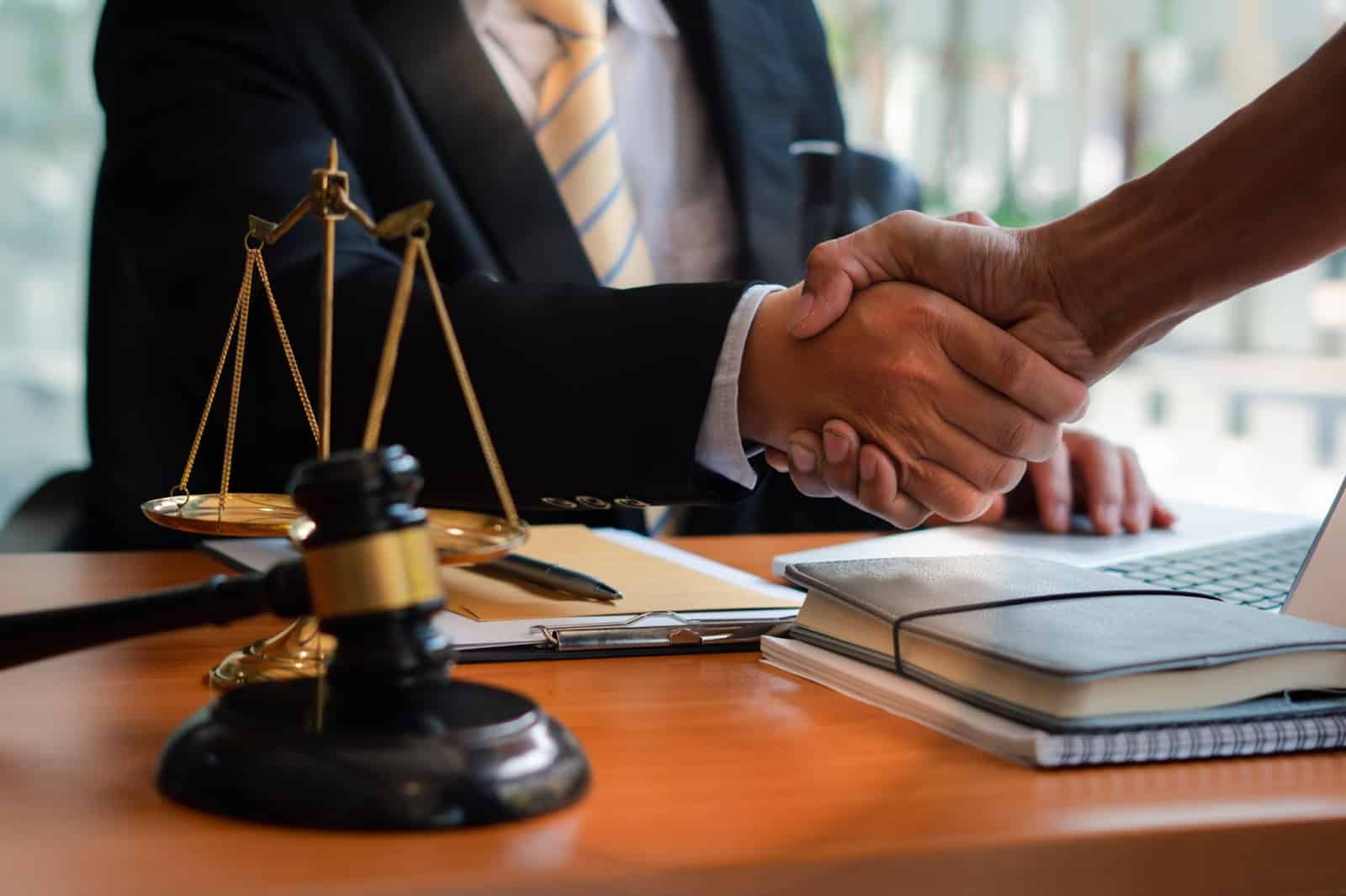 Client and attorney shaking hands over desk with documents, gavel, and justice scales | New Direction Family Law
