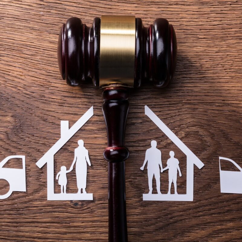 Gavel on wooden table separating paper cutout of house and family | New Direction Family Law