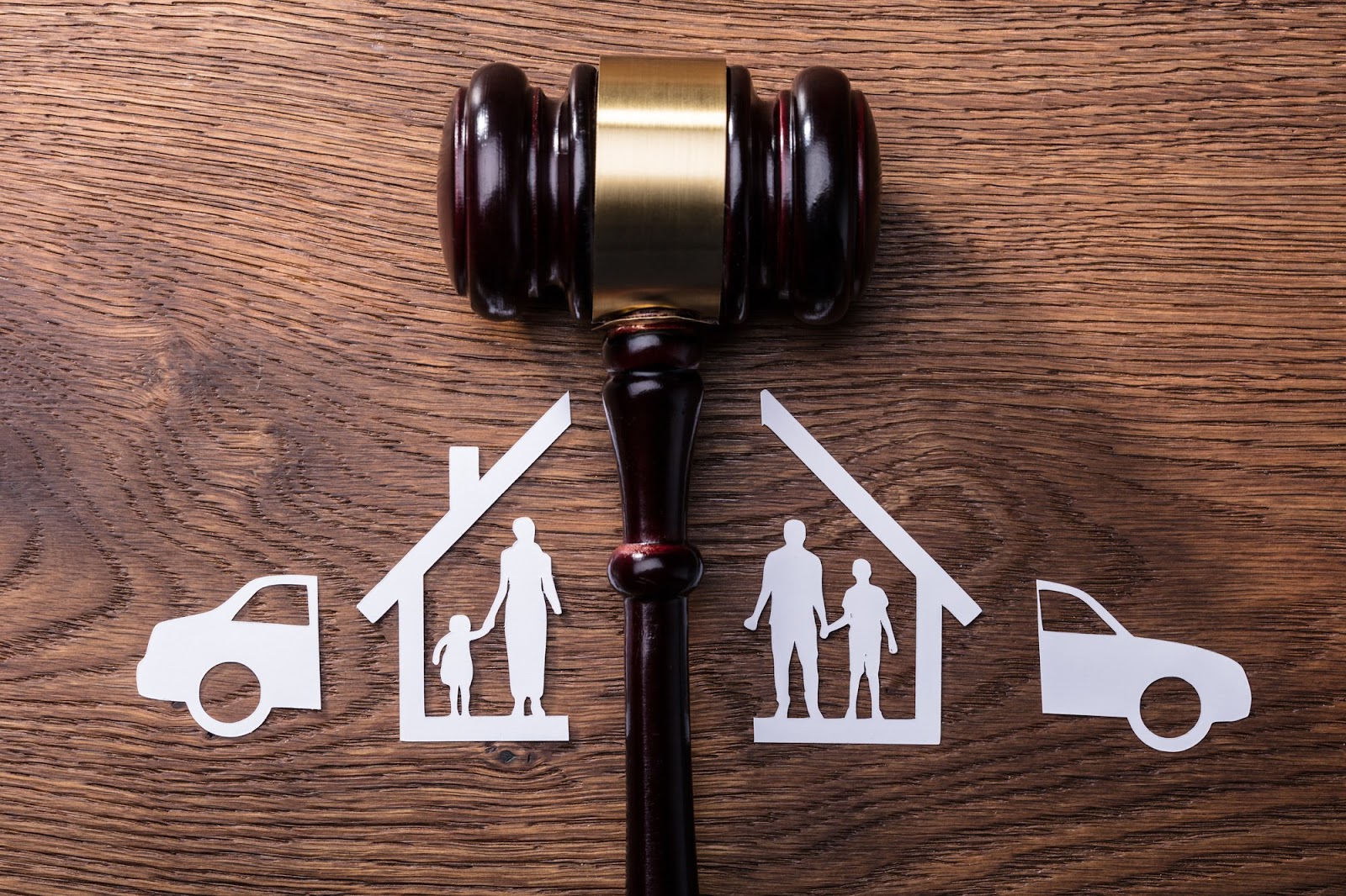 Gavel on wooden table separating paper cutout of house and family | New Direction Family Law