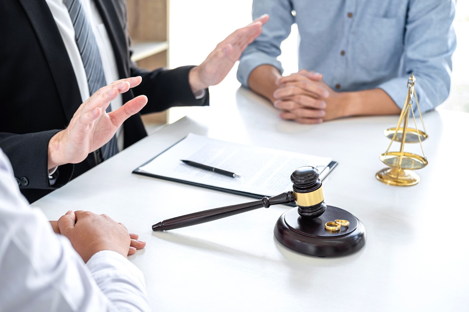 Mediator speaking with two individuals, a gavel, two wedding rings and clipboard between them | New Direction Family Law