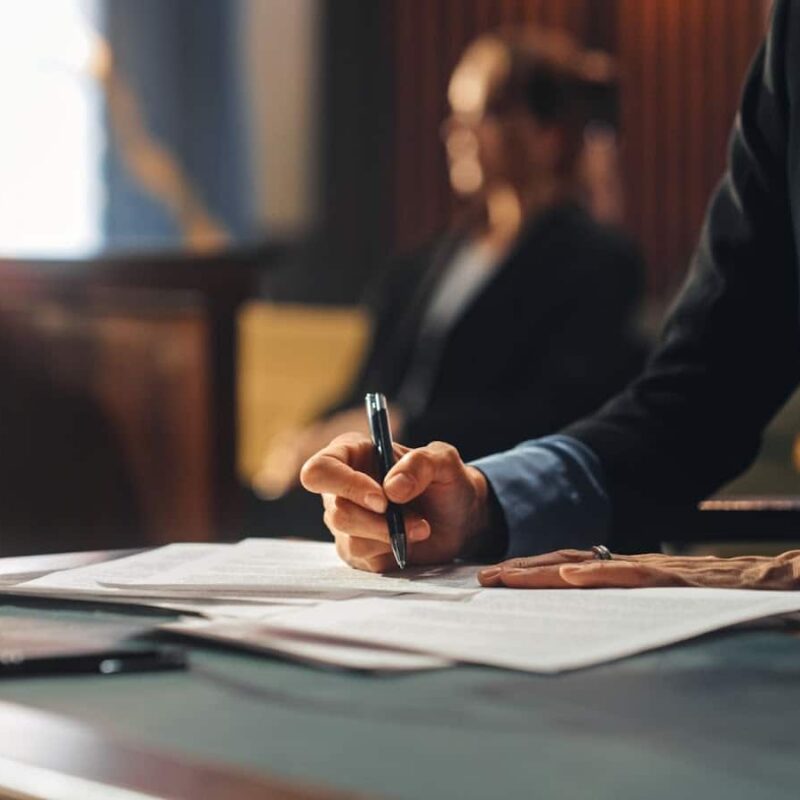 Attorney writing on a legal document with a client in the background. | New Direction Family Law