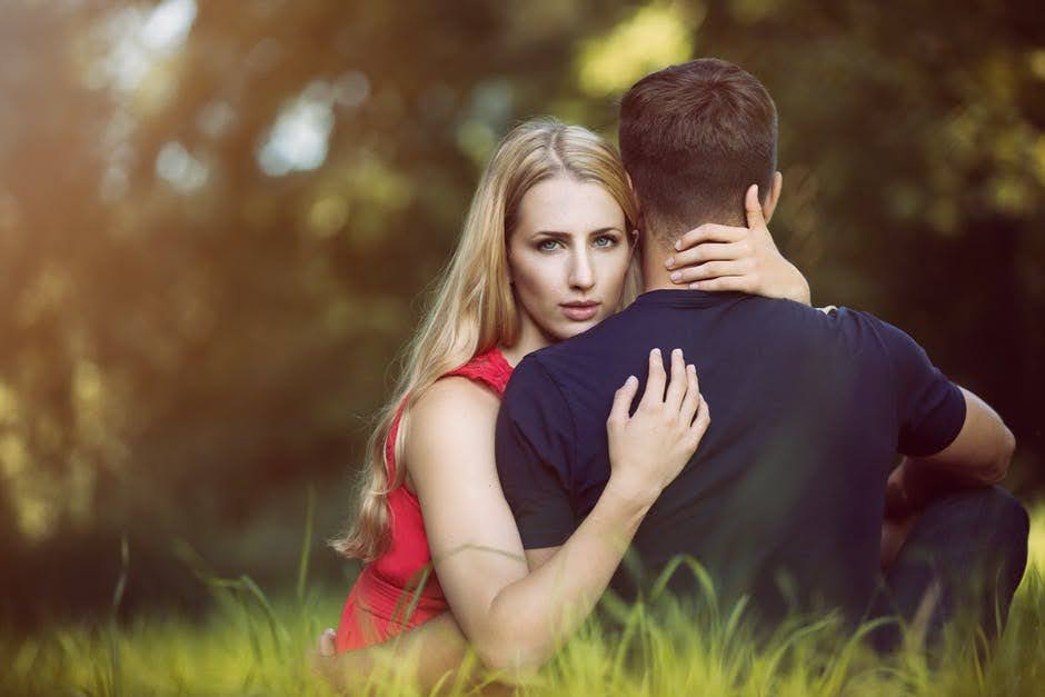 Woman holds husband in nature with a sneaky face.