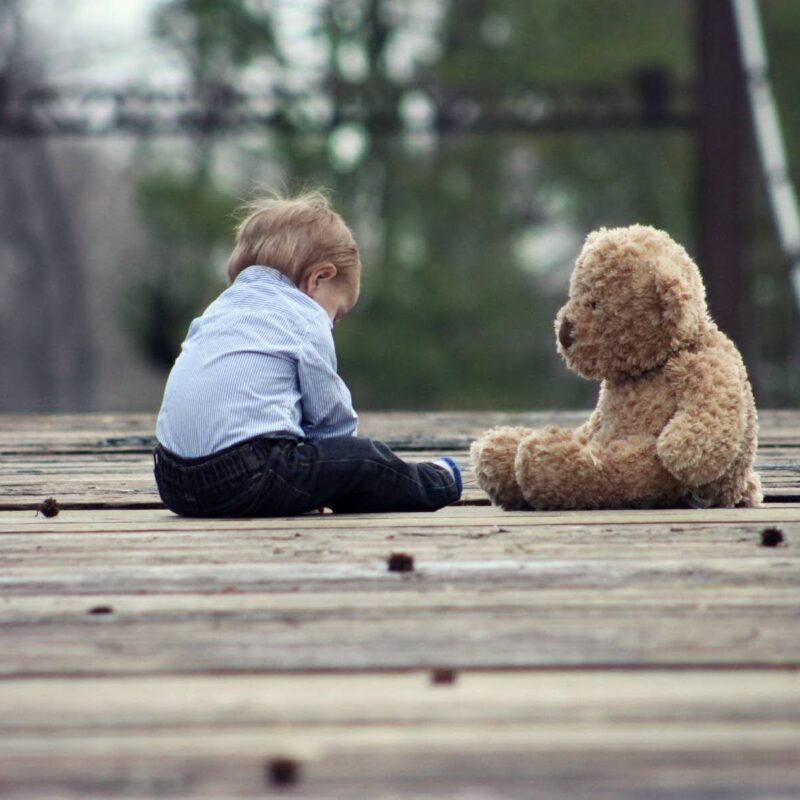Young child sitting alone with a teddy bear. | New Direction Family Law