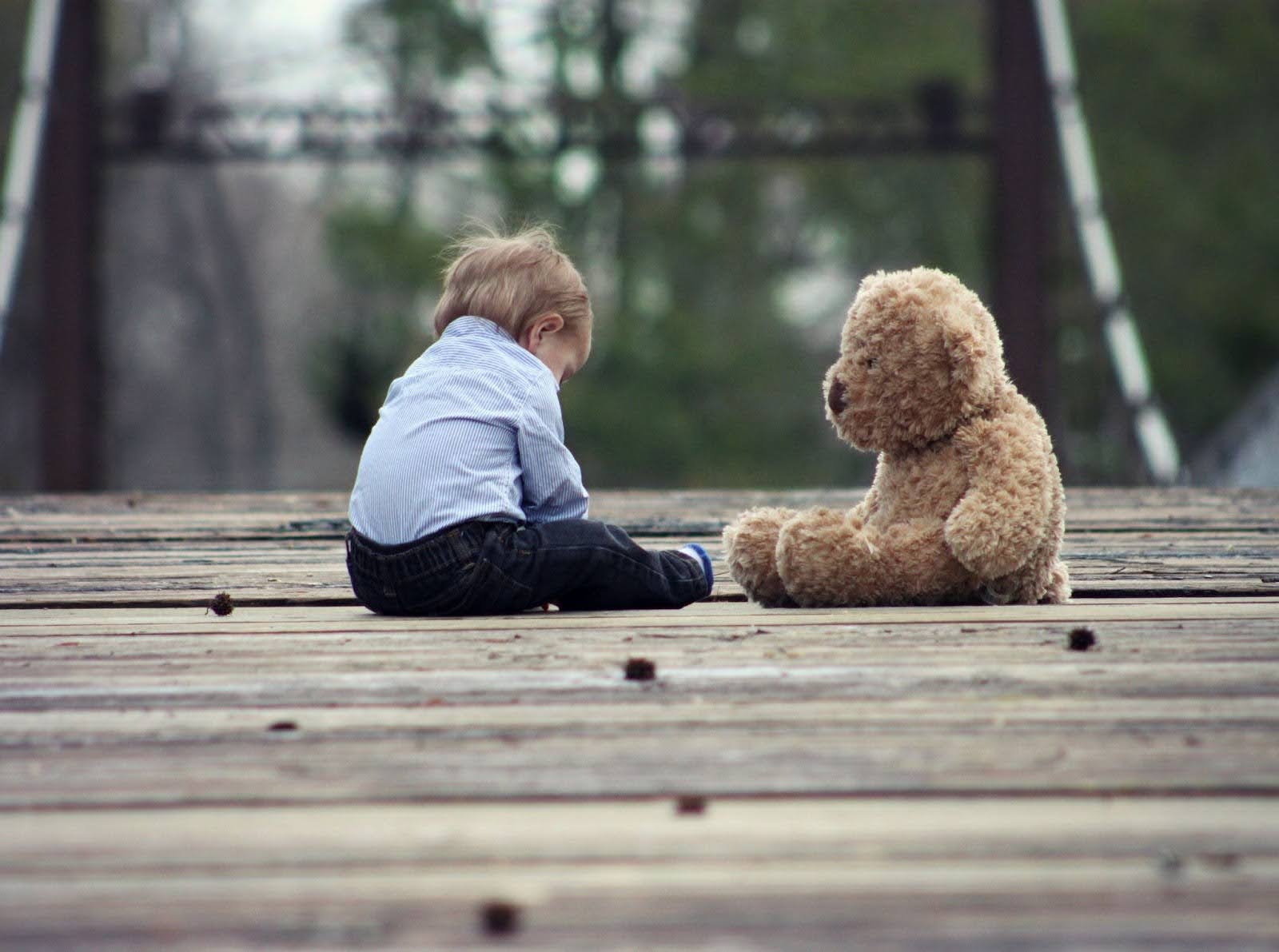 Young child sitting alone with a teddy bear. | New Direction Family Law
