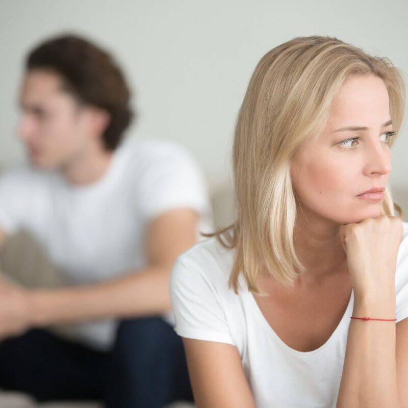 Sad woman looking off with a man sitting behind her. | New Direction Family Law