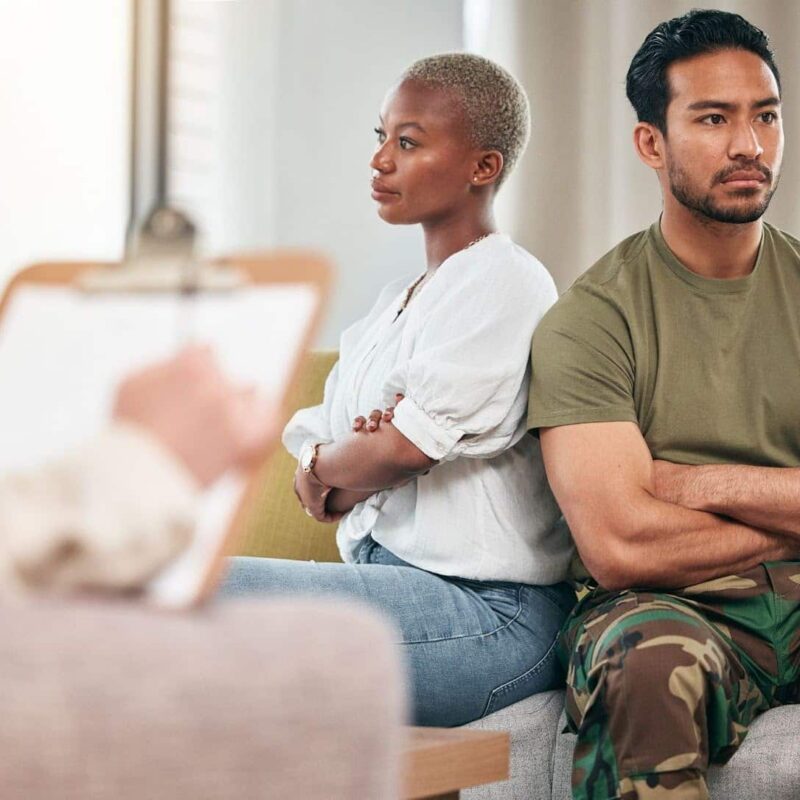 A Military service member and his spouse sitting down with crossed arms and their backs to each other while discussing divorce. | New Direction Family Law