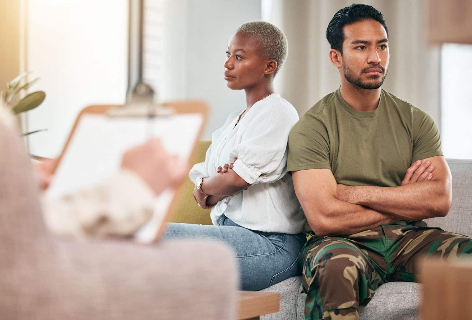A Military service member and his spouse sitting down with crossed arms and their backs to each other while discussing divorce. | New Direction Family Law