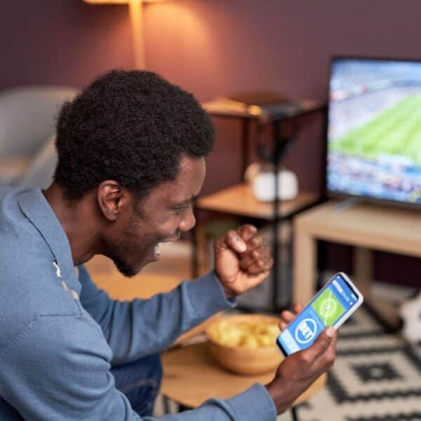 A side view of a man holding a smartphone with online sports betting app and cheering. | New Direction Family Law