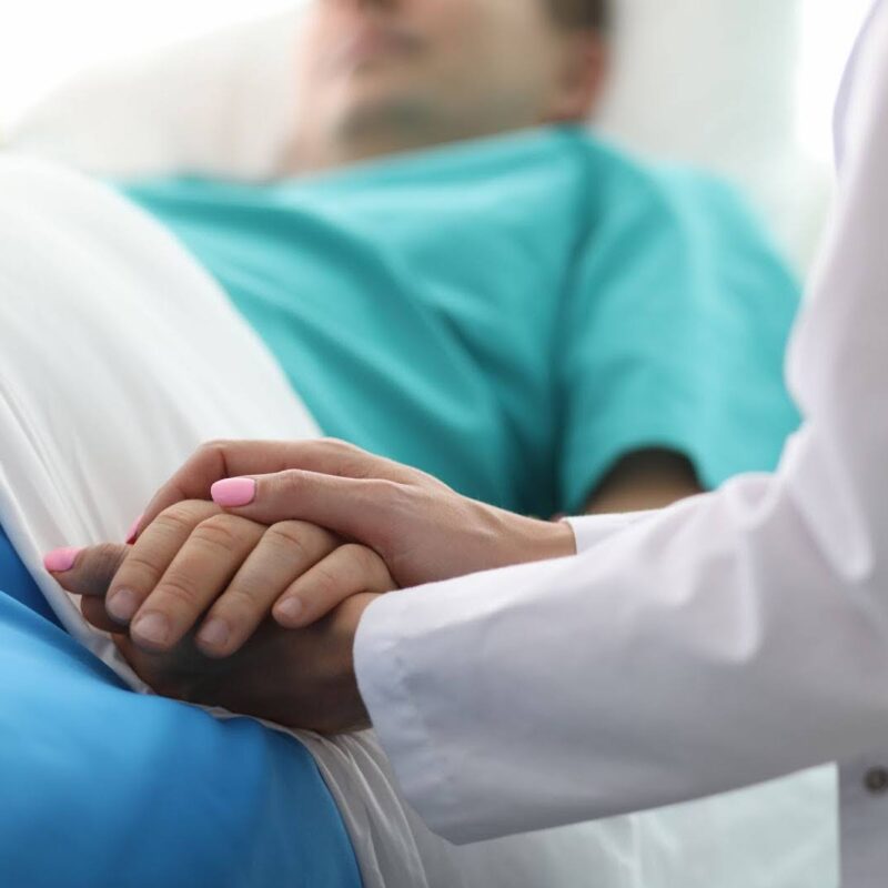 Doctor holding a patient’s hand in hospital room. | New Direction Family Law