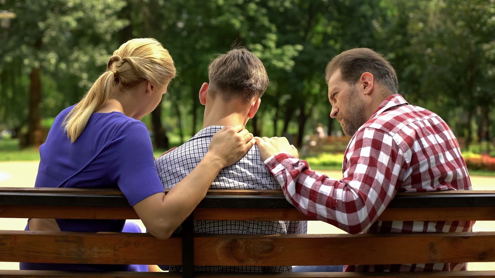 Parents consoling young adult son on a park bench | New Direction Family Law