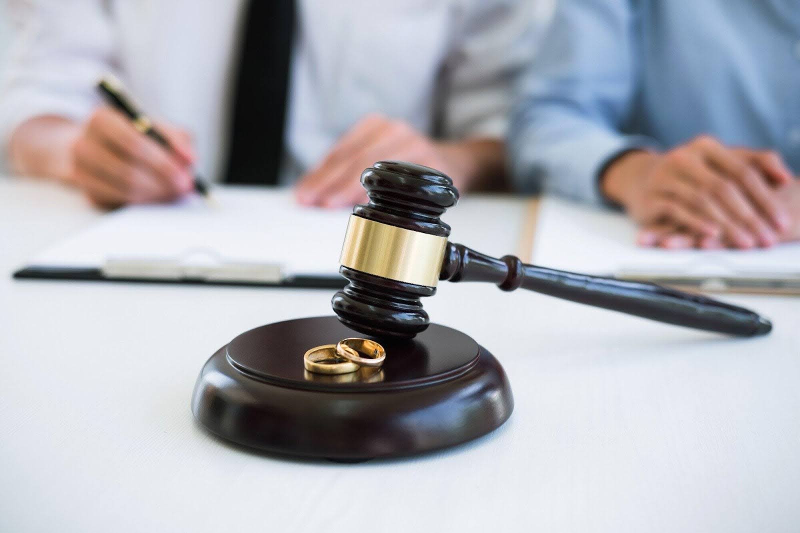 Gavel with two wedding rings and divorce papers. | New Direction Family Law